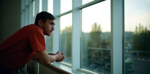 A man sitting in front of a window looking out.