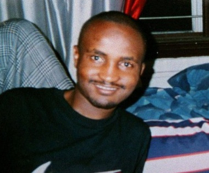 A man smiling for the camera in front of a bed.