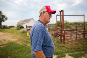 A man in blue shirt wearing red hat near fence.