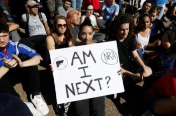 A woman holding up a sign that says am i next ?