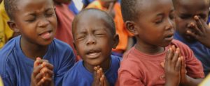 A young boy is praying in front of other children.