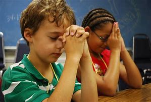 Two children sitting at a table with their hands folded together.