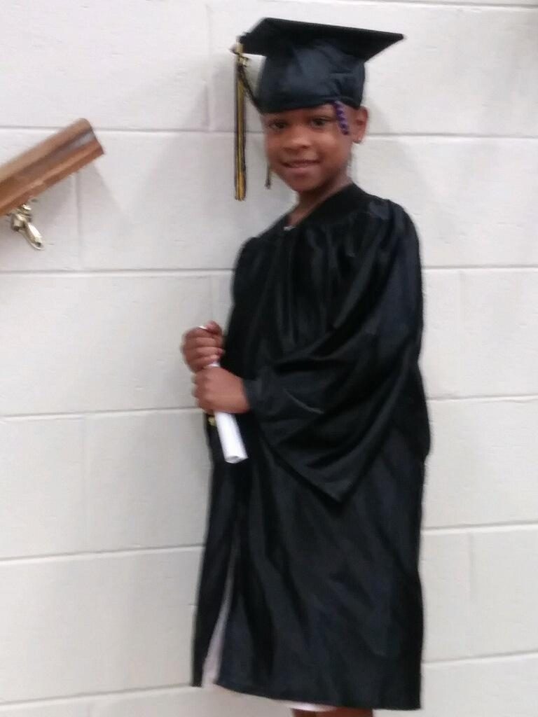 A young boy in graduation attire holding his cap and robe.