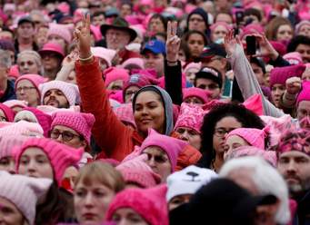 A crowd of people wearing pink hats and holding up peace signs.