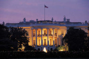 A white house lit up at night with trees in front.