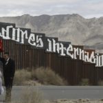 A man and woman standing in front of the border fence.