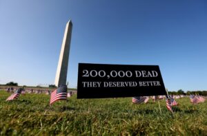 A sign in the grass with american flags and a monument.